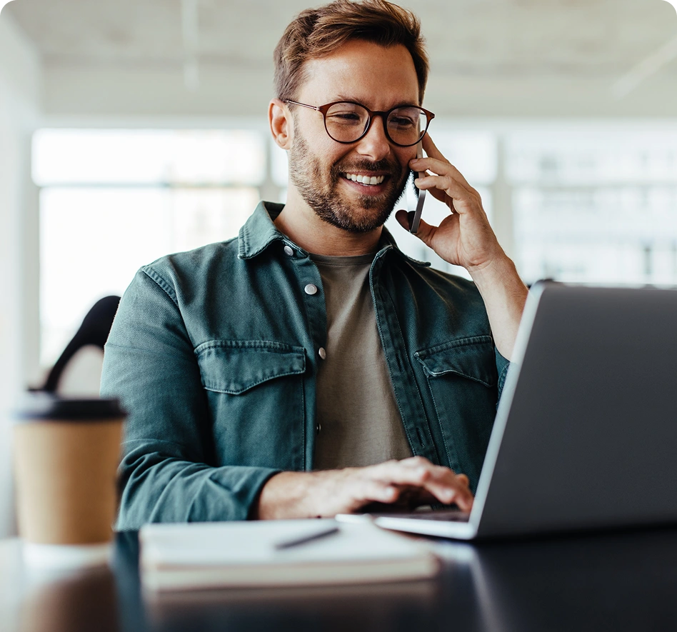 Mann mit Brille, der lächelnd am Laptop arbeitet und dabei telefoniert.