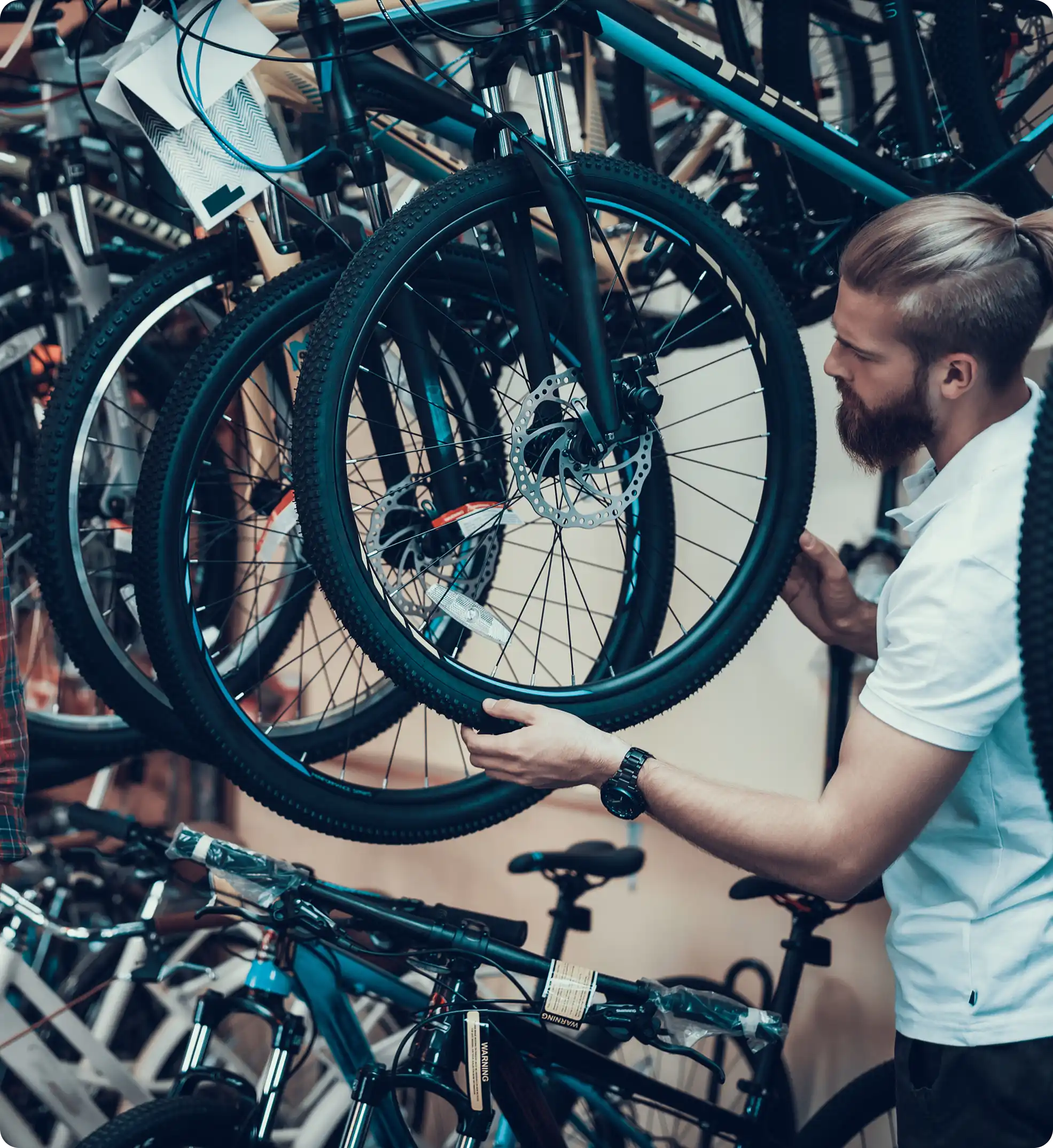 Mann prüft Reifen eines Mountainbikes in einem Fahrradgeschäft mit mehreren Fahrrädern im Hintergrund.