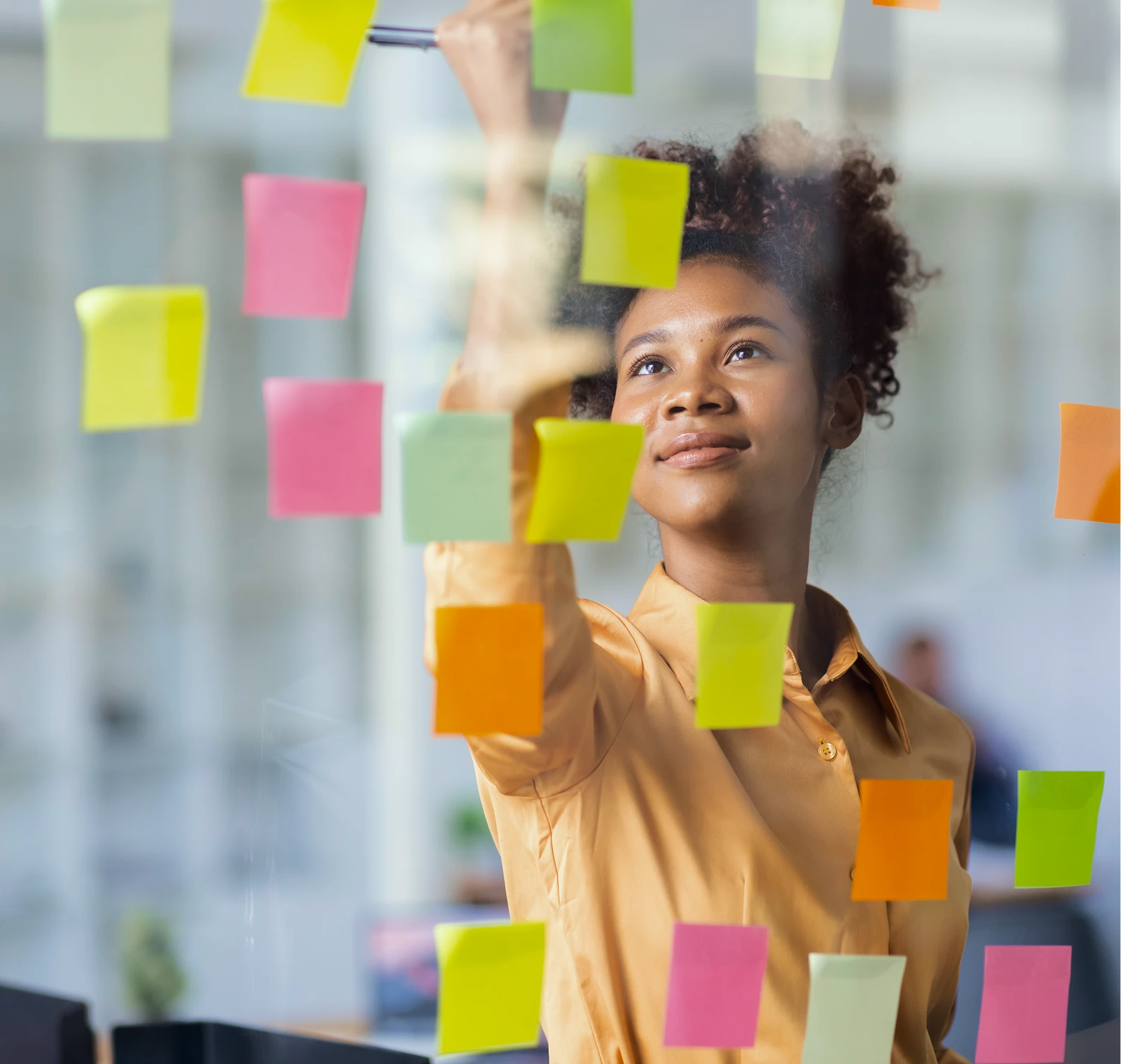 Frau schreibt bunte Haftnotizen an eine Glaswand in einem modernen Büro.