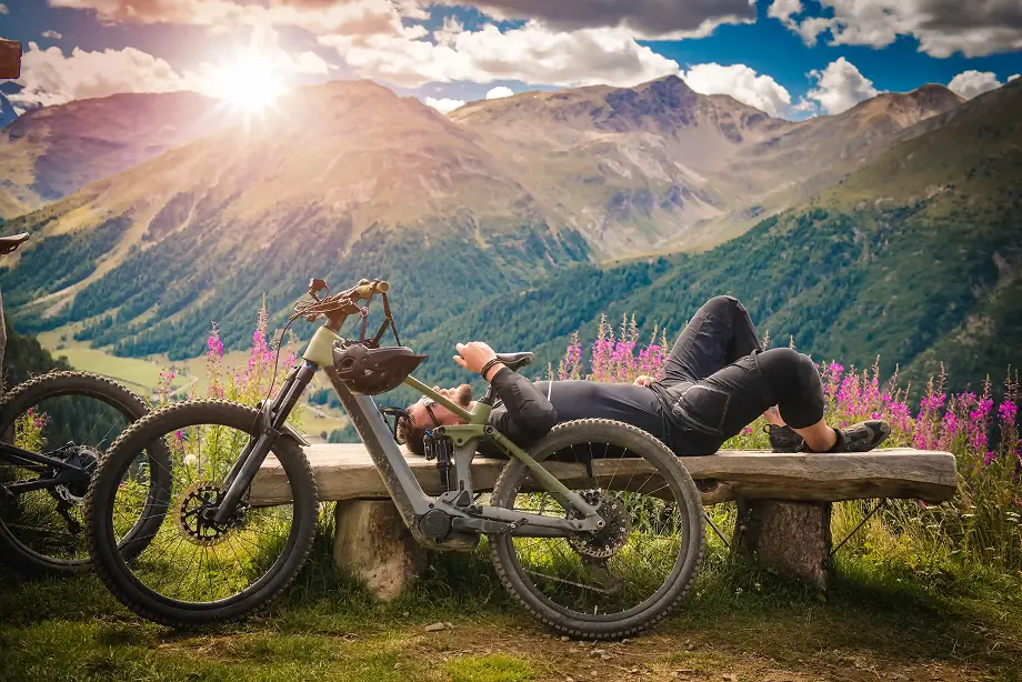A man is laying on a bench with a bicycle next to him.