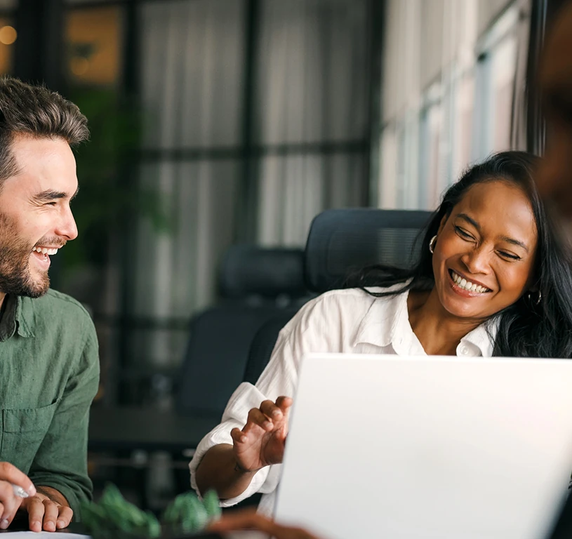 A man and woman are sitting in front of a laptop.
