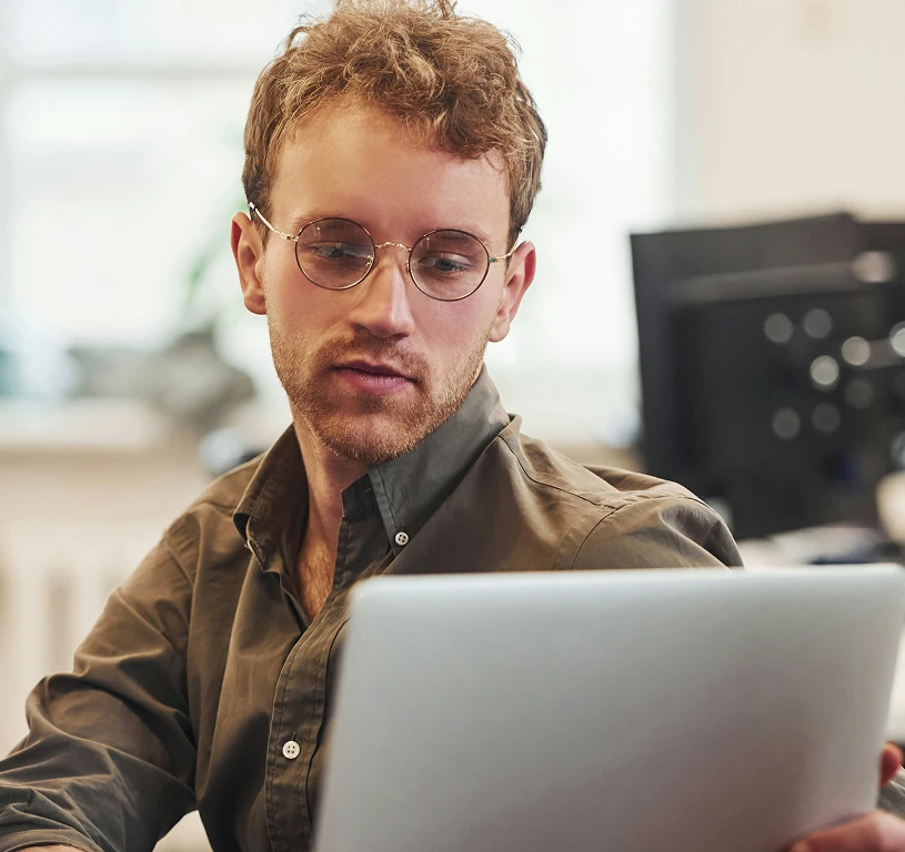 A man wearing glasses and a brown shirt is looking at a laptop.