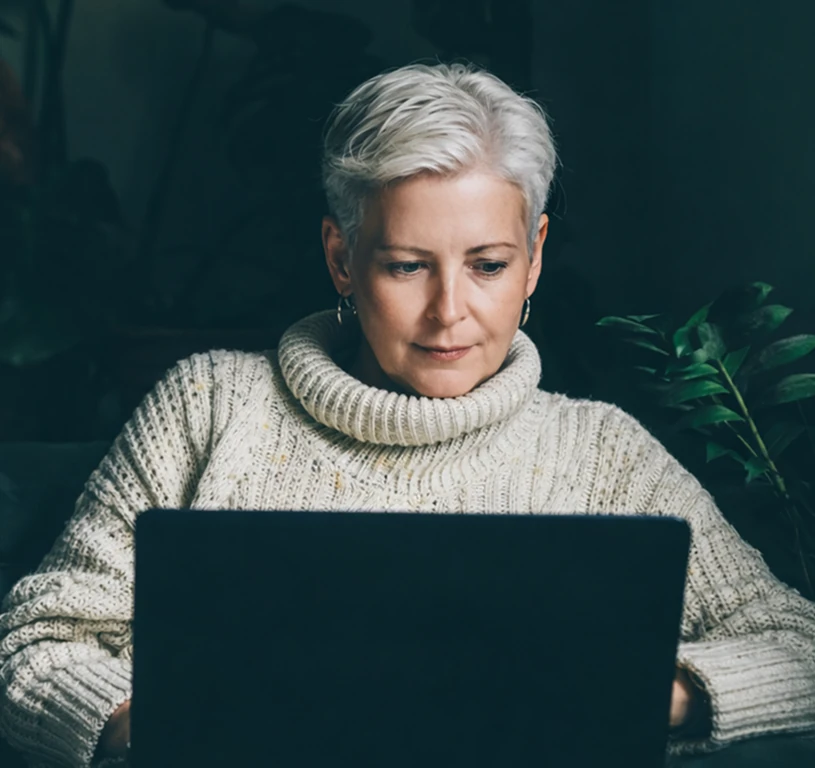 A woman with blonde hair is sitting in front of a laptop.