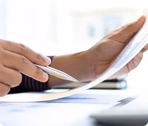 Person holding a pen and reviewing printed documents with charts.