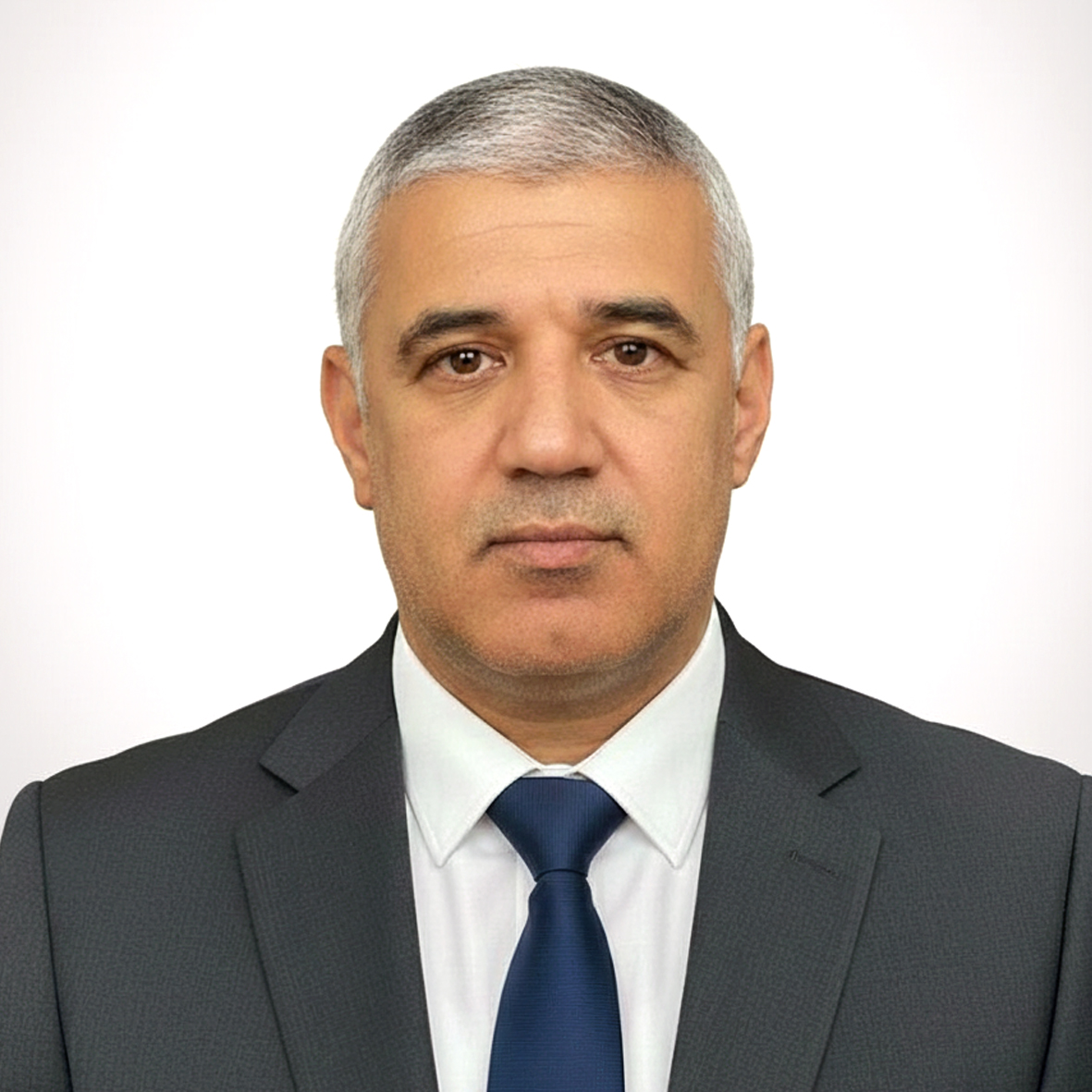 Middle-aged man with short gray hair wearing a dark suit, white shirt, and blue tie, facing forward with a neutral expression.