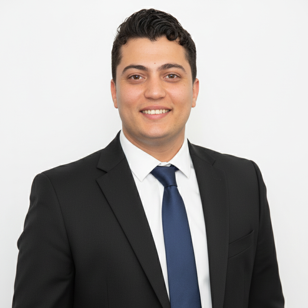 Young man smiling, wearing a black suit jacket and white shirt, with arms crossed.