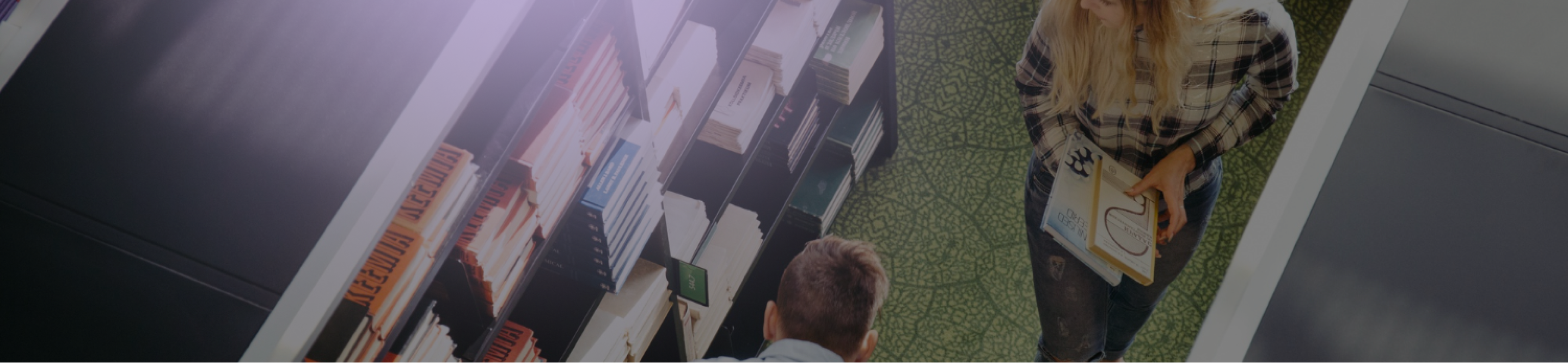Overhead view of a woman holding documents standing on a green patterned floor next to a man and bookshelves filled with books.