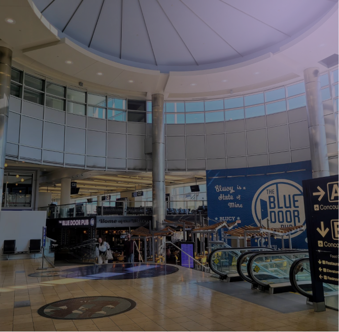 Interior of an airport terminal with a high dome ceiling, a Blue Door Pub restaurant, escalators, and directional signs for concourses.