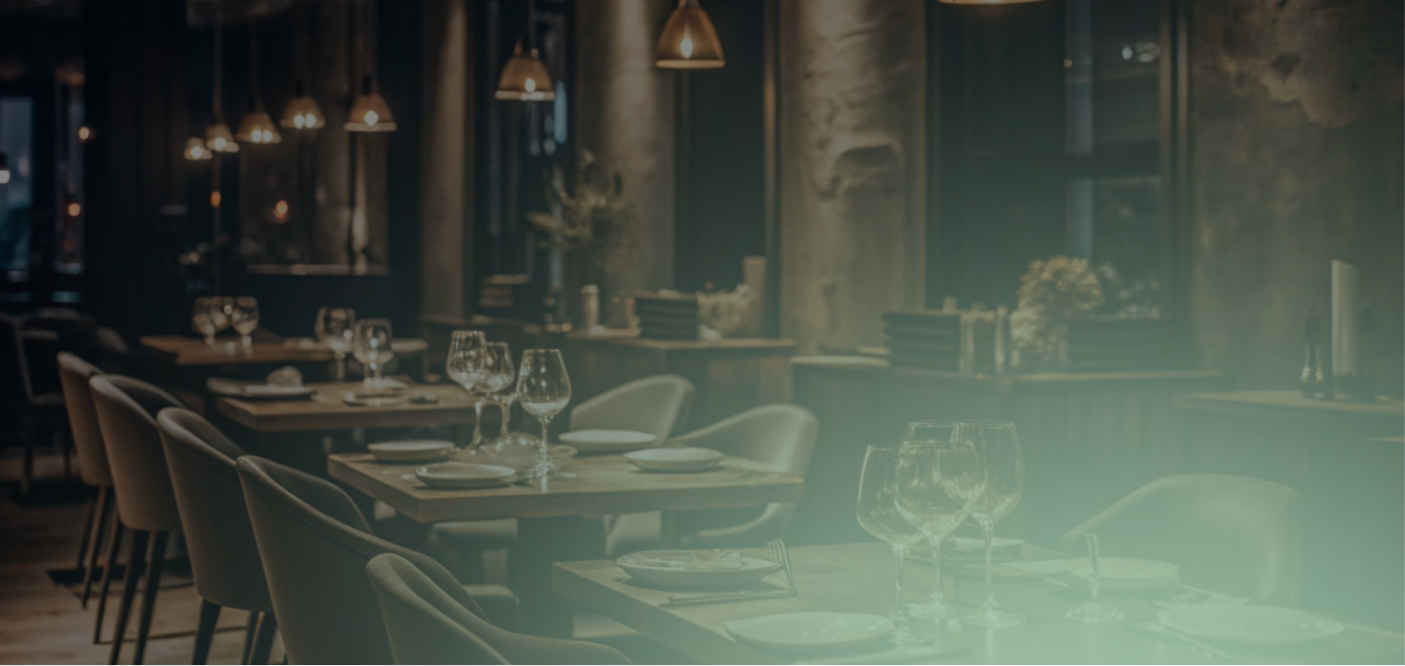 Dimly lit restaurant interior with wooden tables set with plates and wine glasses, surrounded by upholstered chairs.