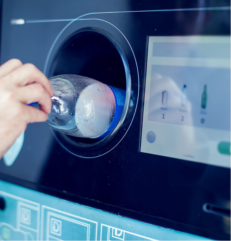 Hand inserting a plastic bottle into a recycling machine with a digital display screen.