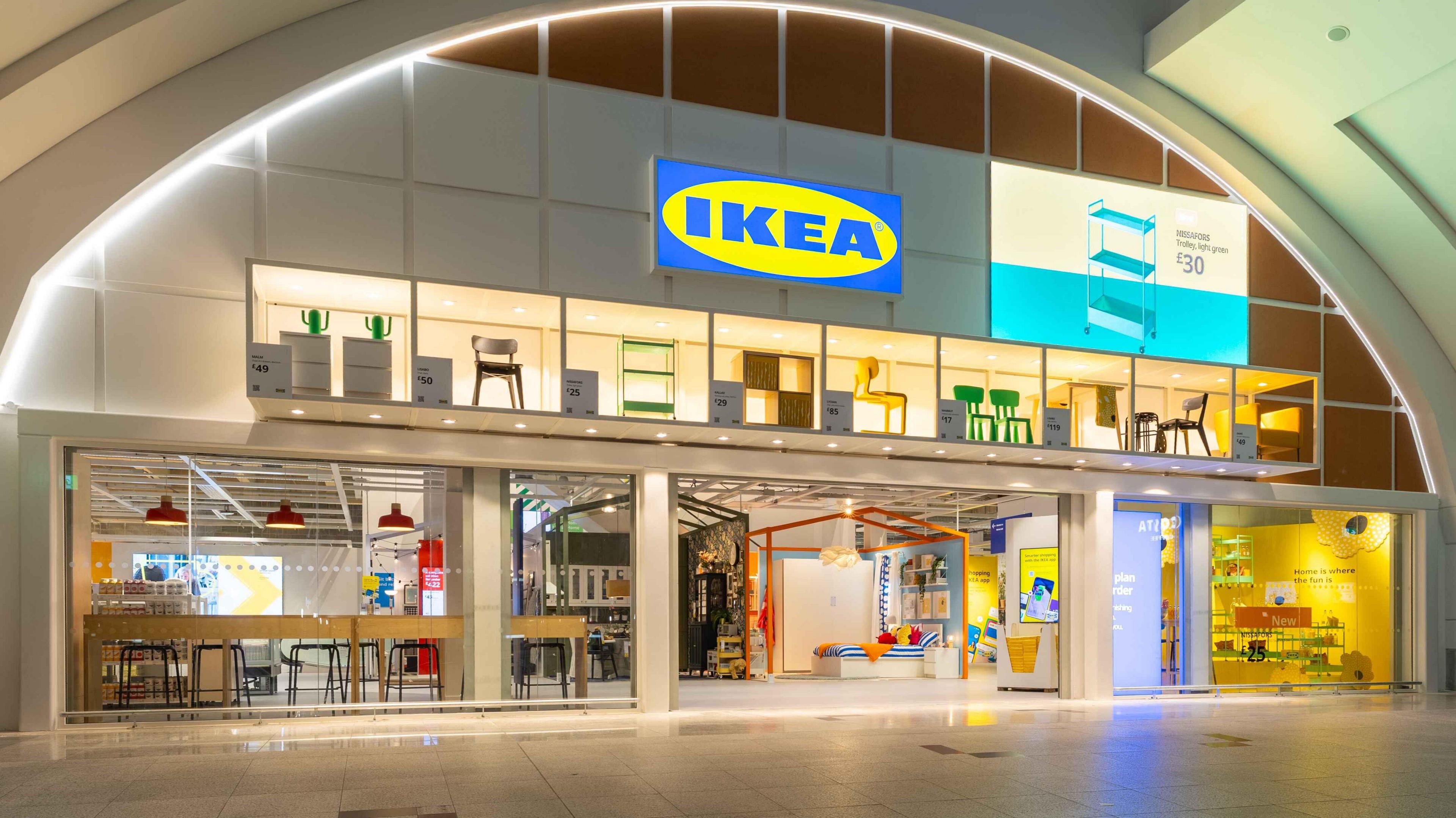 Illuminated IKEA store front with furniture displays, including chairs and shelving units, inside a modern shopping mall.