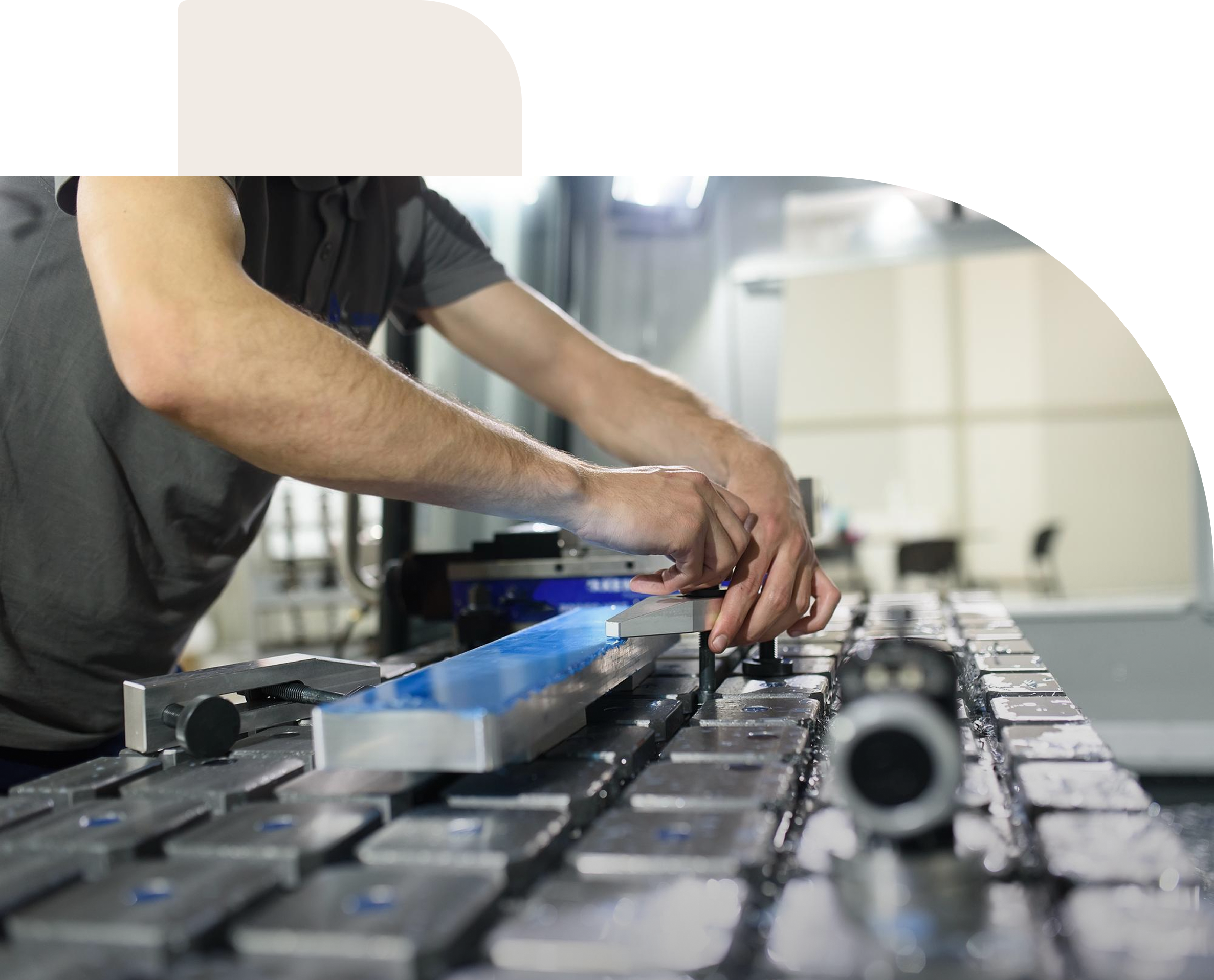 Person using a metalworking machine to clamp a rectangular blue and silver metal piece on a large industrial table.