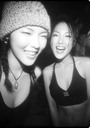 Black and white photo of two young women smiling and posing closely together at a social gathering.