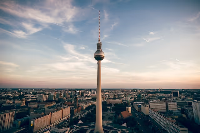 Berühmter Berliner Fernsehturm bei Sonnenuntergang mit Stadtlandschaft im Hintergrund.