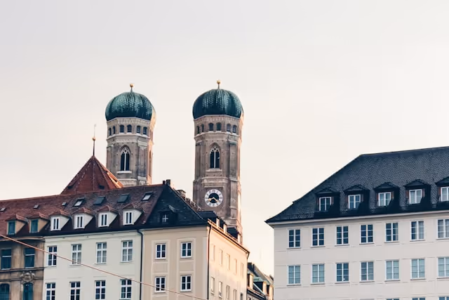 Zwei Türme der Frauenkirche mit grünen Kuppeln hinter alten Gebäuden in München.