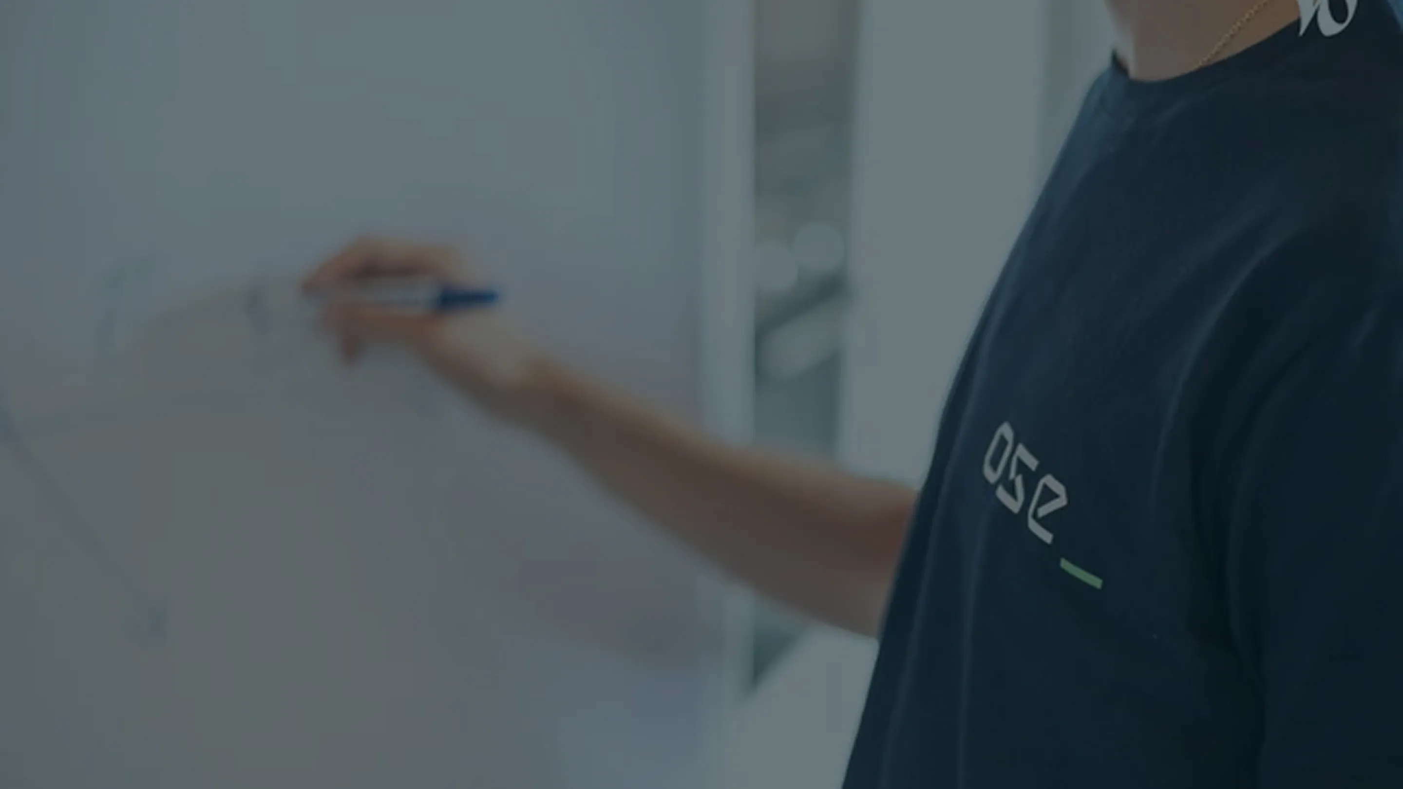 Personne écrivant sur un tableau blanc avec un marqueur bleu, portant un t-shirt bleu marine.