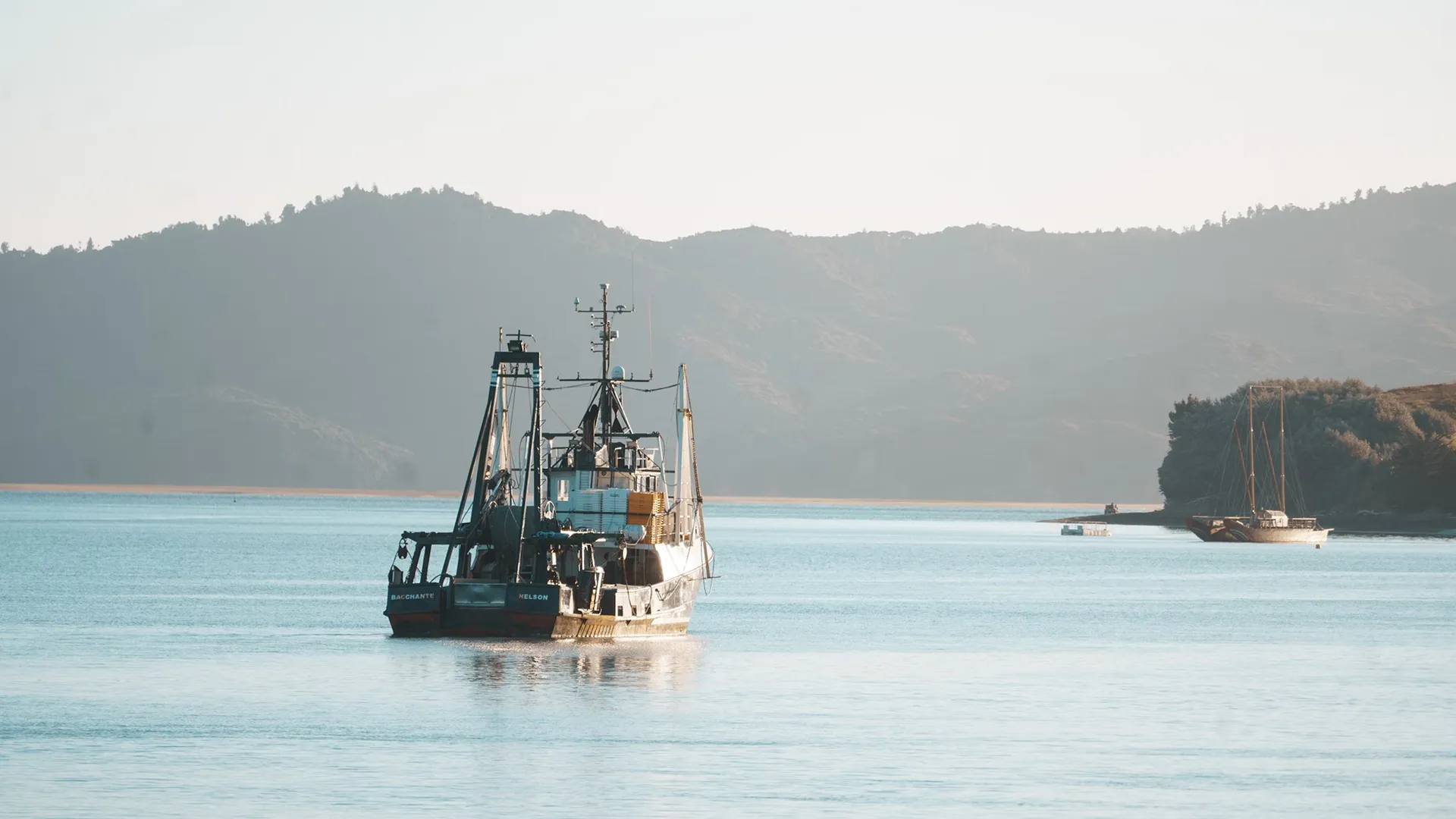 Bateau de pêche ancré sur une mer calme avec des montagnes en arrière-plan sous un ciel clair.