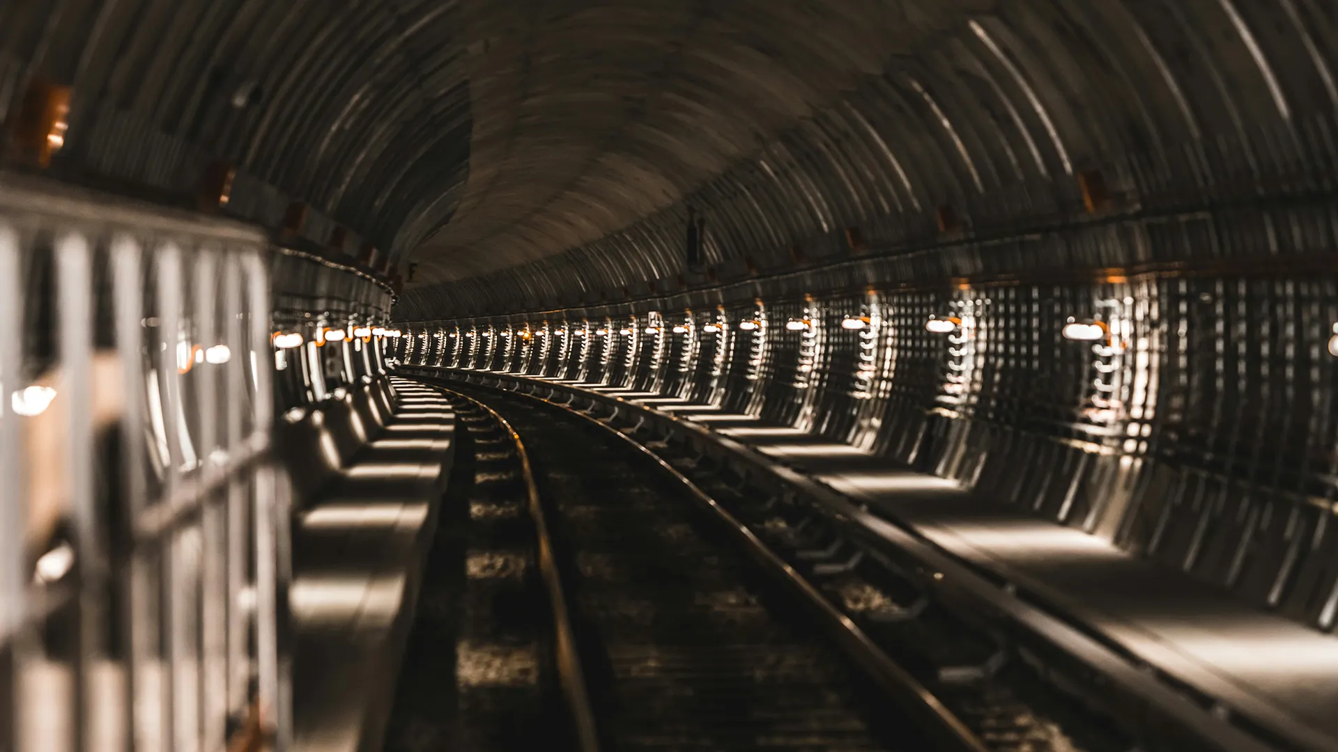 Tunnel ferroviaire courbé éclairé par des lampes murales uniformément espacées.