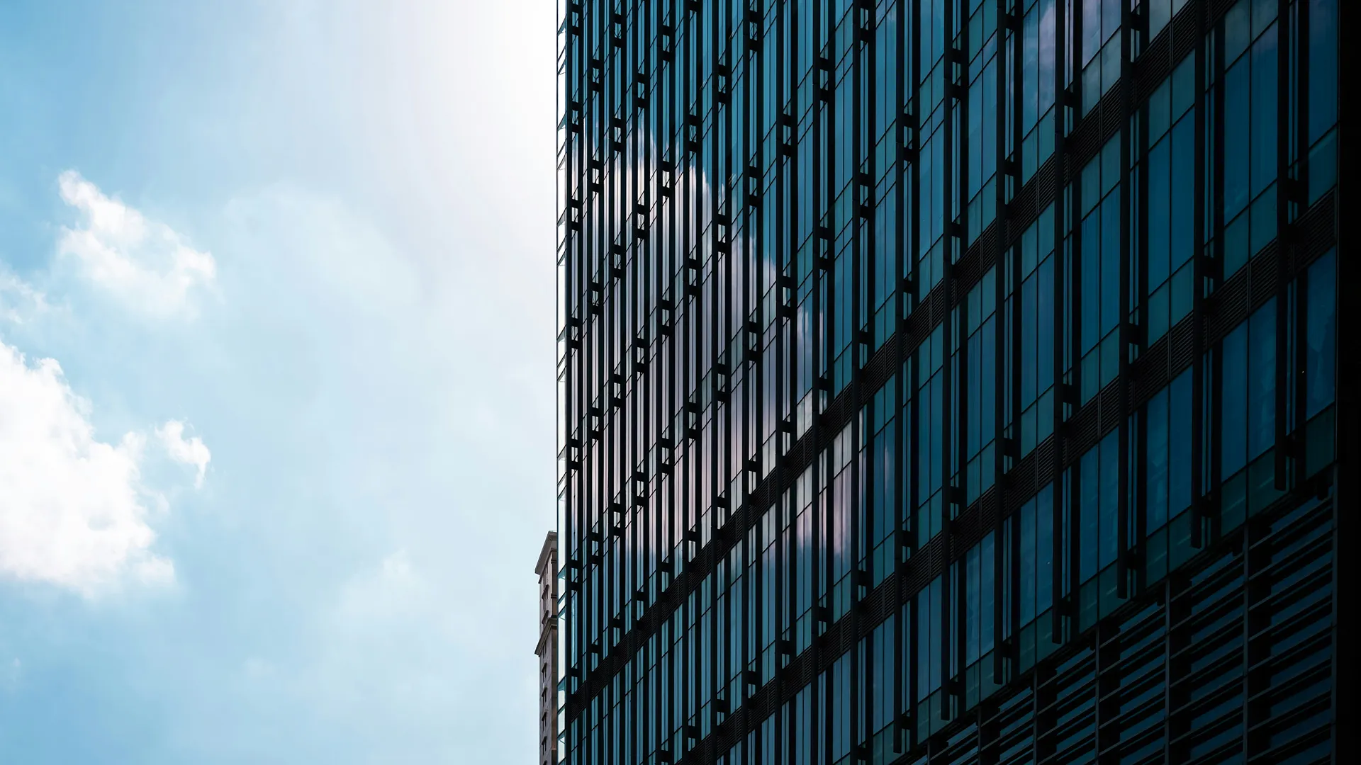 Façade vitrée d'un bâtiment moderne reflétant des nuages dans un ciel bleu.