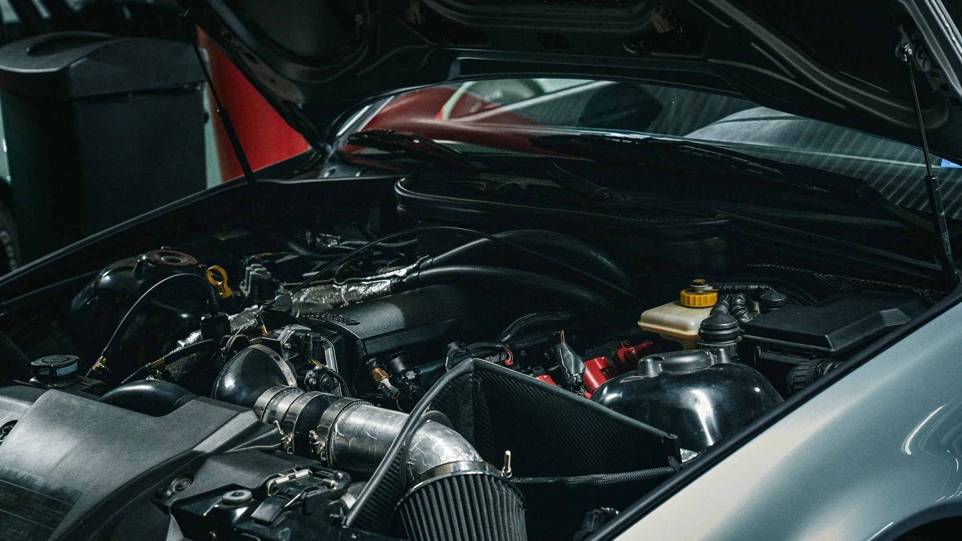 Moteur de voiture moderne avec capot ouvert et composants visibles sous la lumière tamisée.