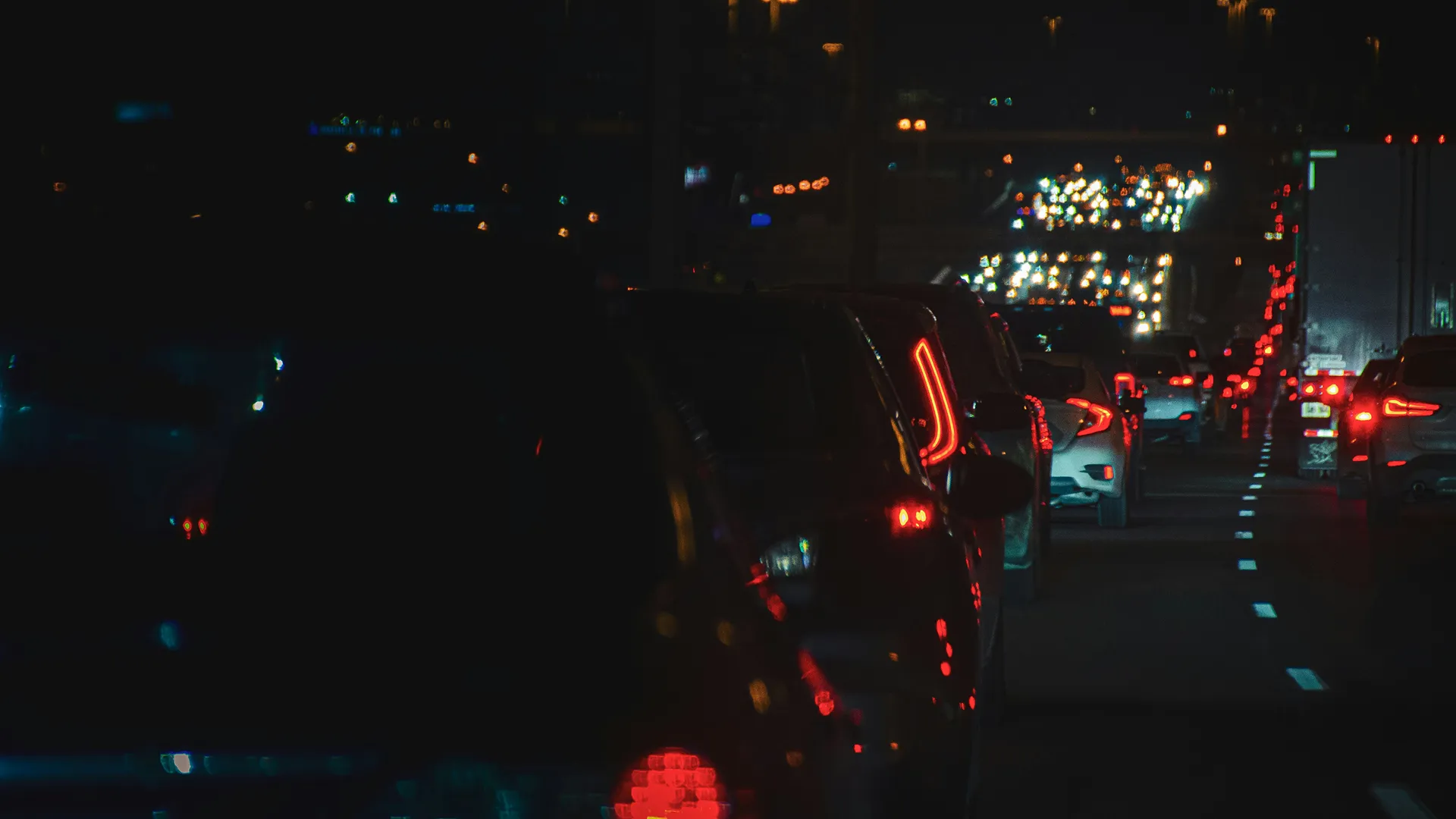 Feux arrière de voitures dans un embouteillage nocturne sur une autoroute avec des lumières floues au loin.