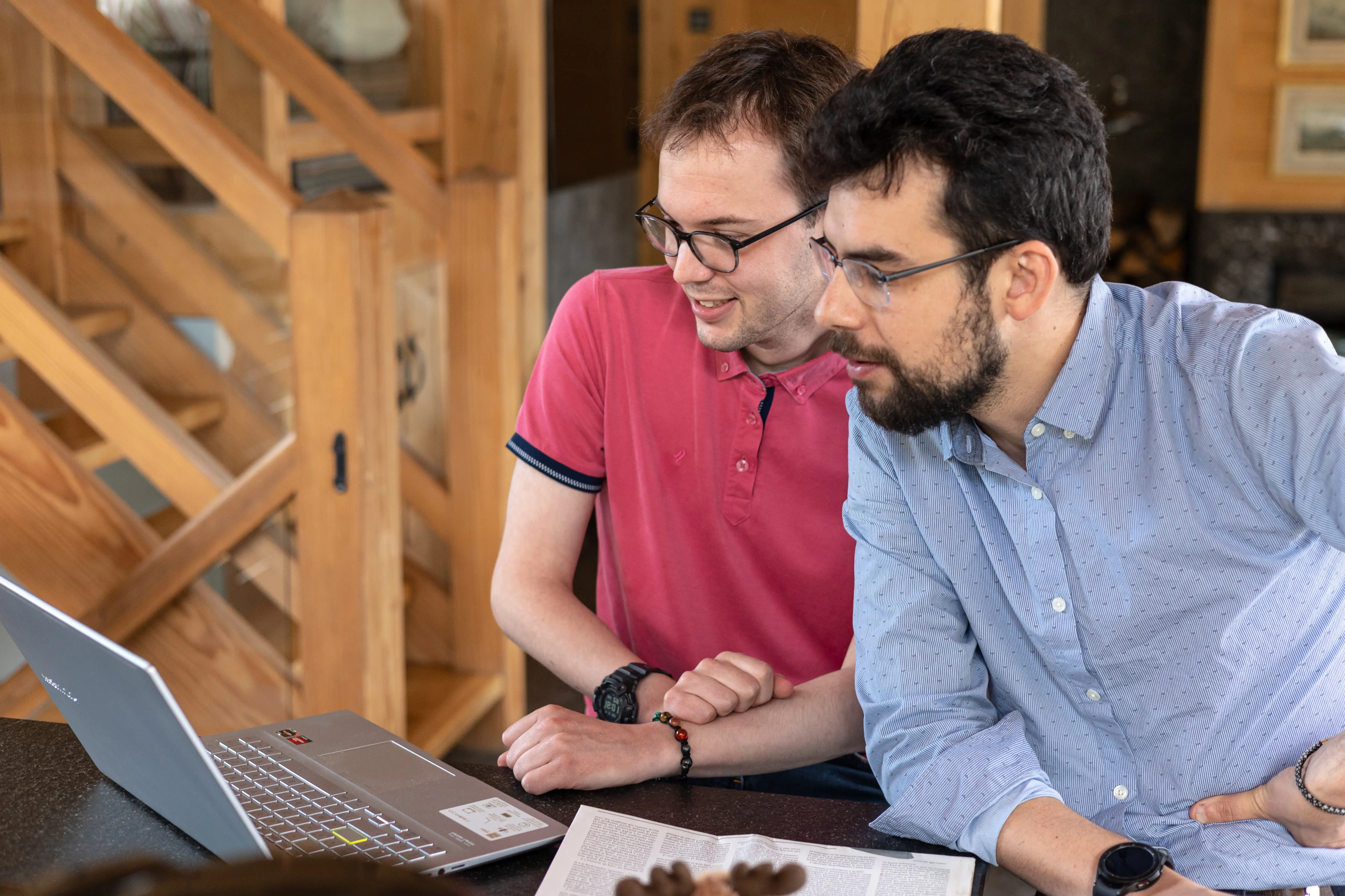 Trois personnes concentrées collaborant devant un ordinateur portable dans une salle lumineuse avec une fenêtre en arrière-plan.