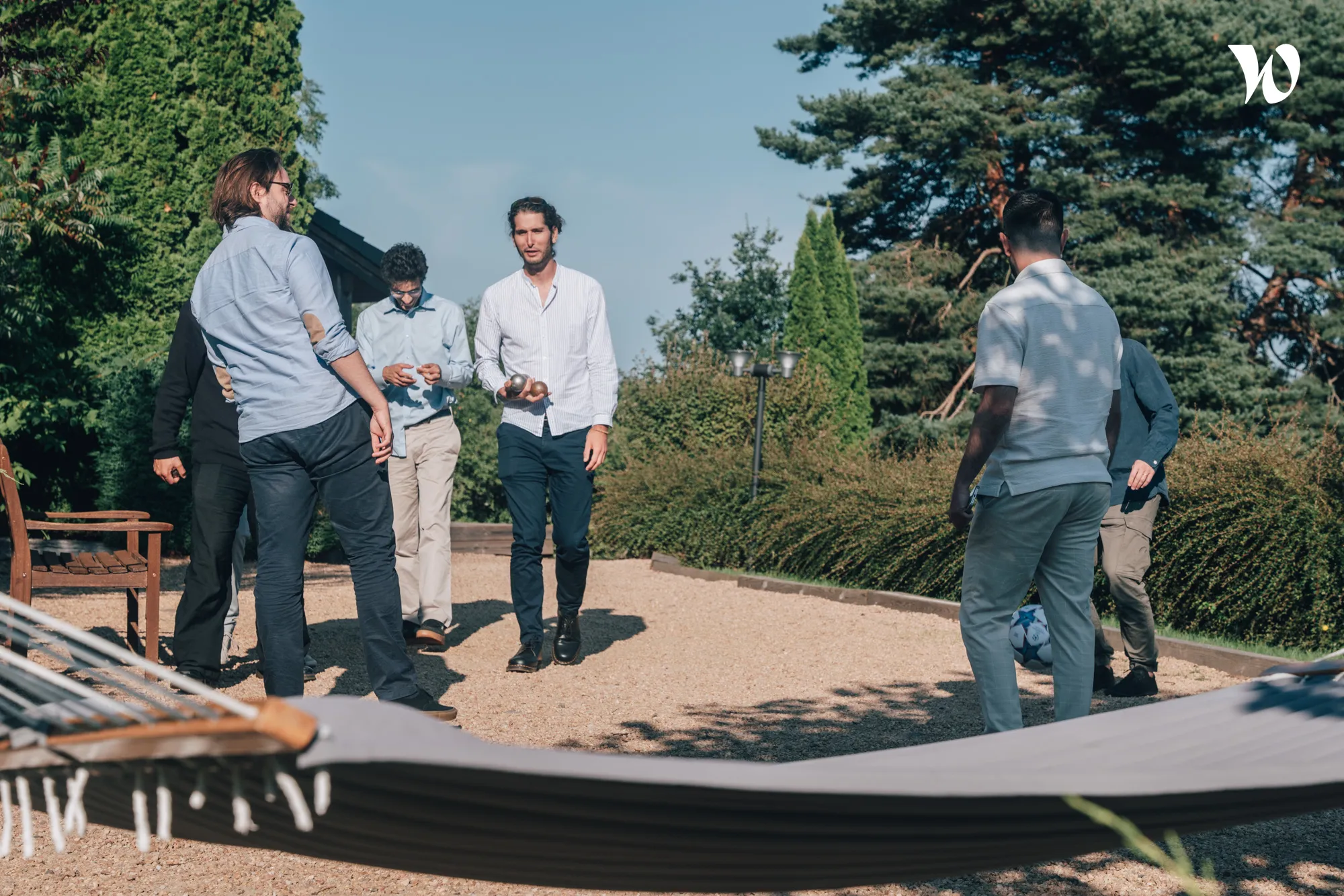 Un groupe d'hommes joue à la pétanque en plein air dans un jardin sous un ciel bleu.