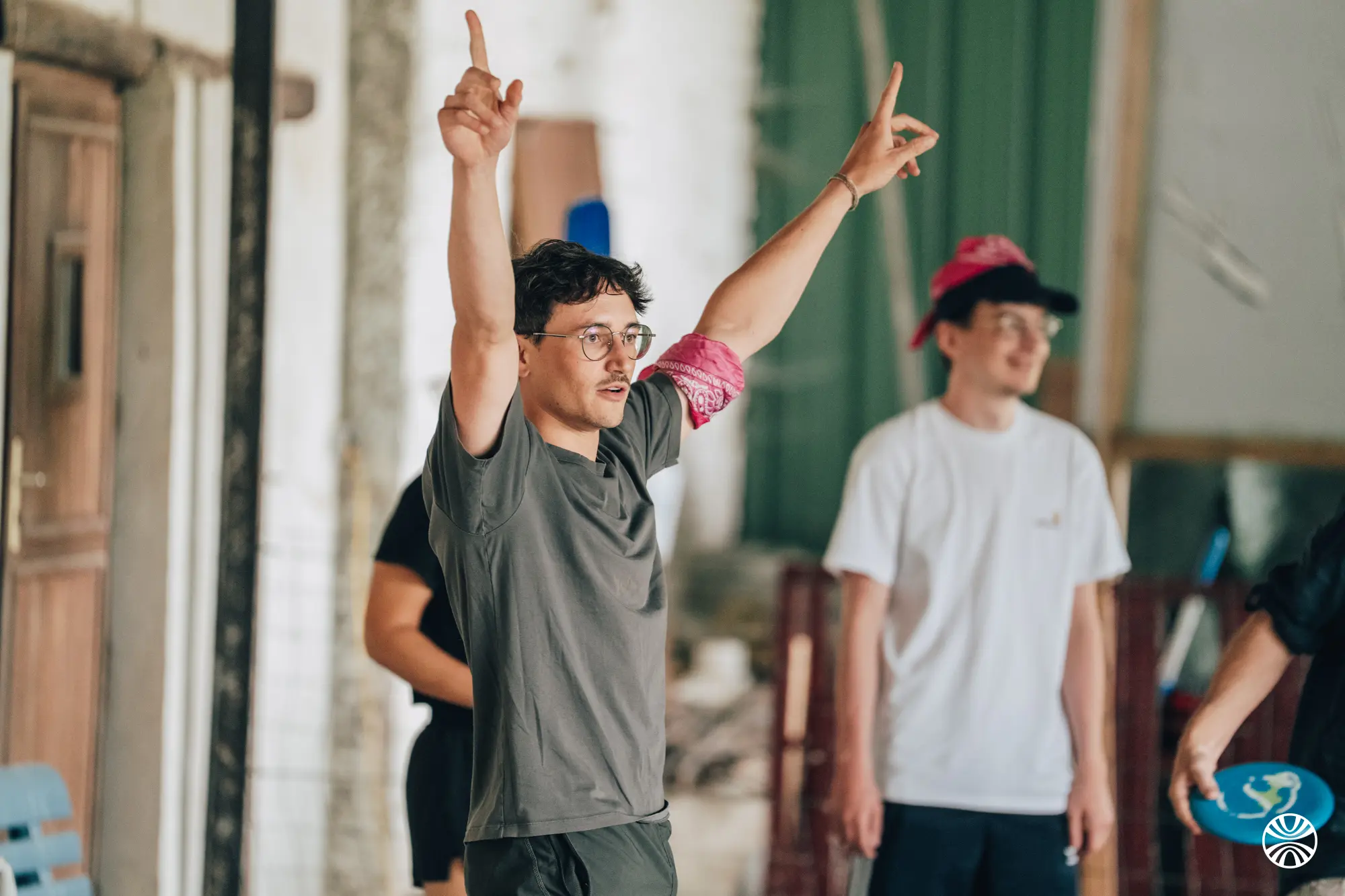 Cinq hommes en discussion décontractée à l'extérieur, devant un bâtiment en bois avec bancs et chaises en bois.