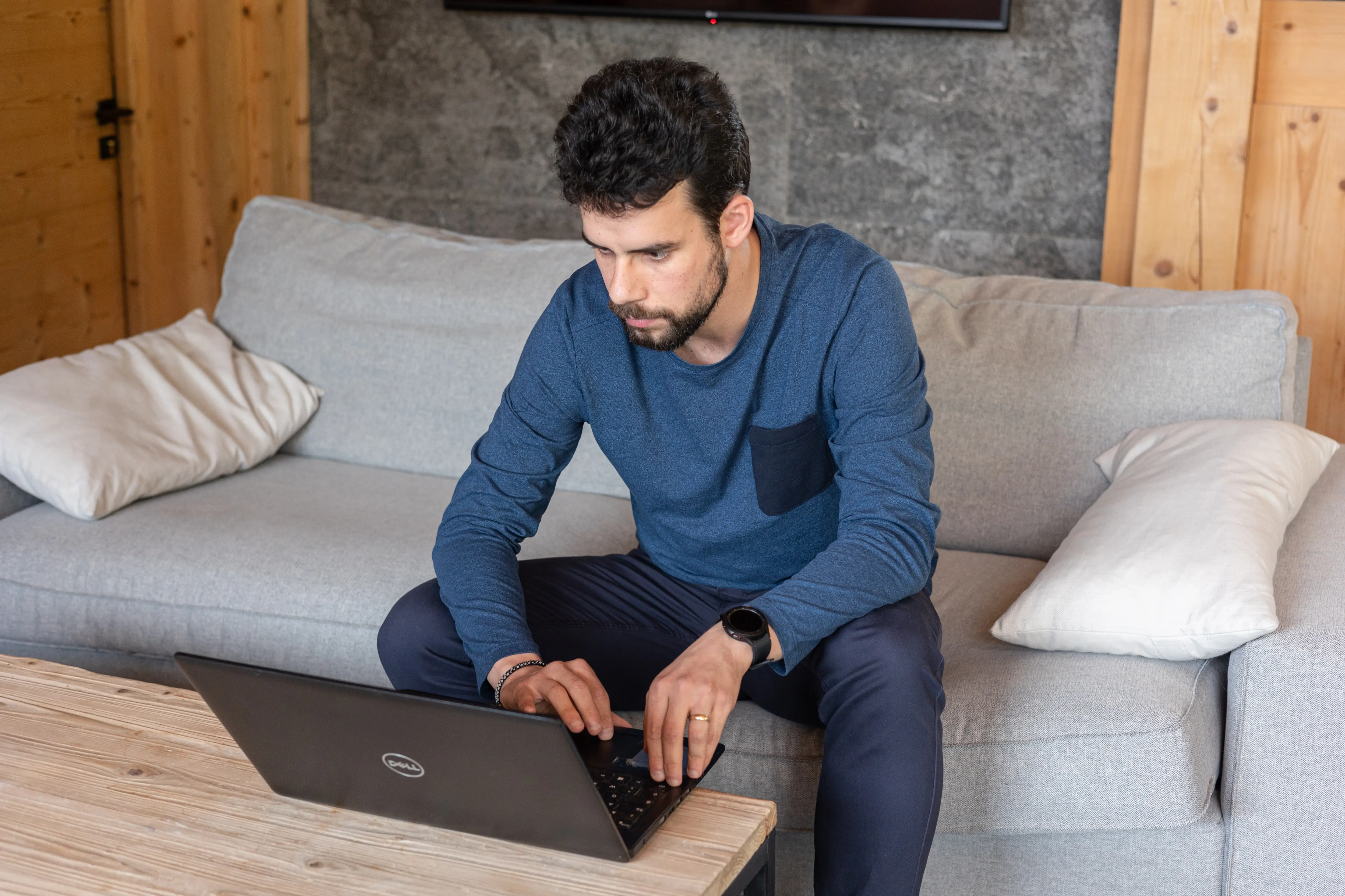 Deux hommes discutant sur une terrasse en bois avec des verres à la main, entourés de végétation et de montagnes enneigées en arrière-plan.