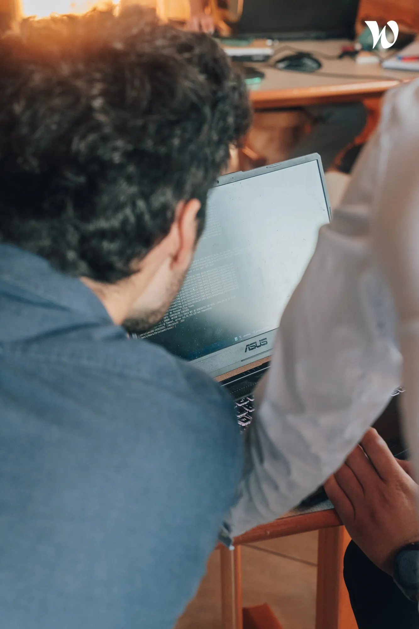 Deux personnes regardant un ordinateur portable Asus avec des lignes de code à l'écran dans un environnement de bureau.