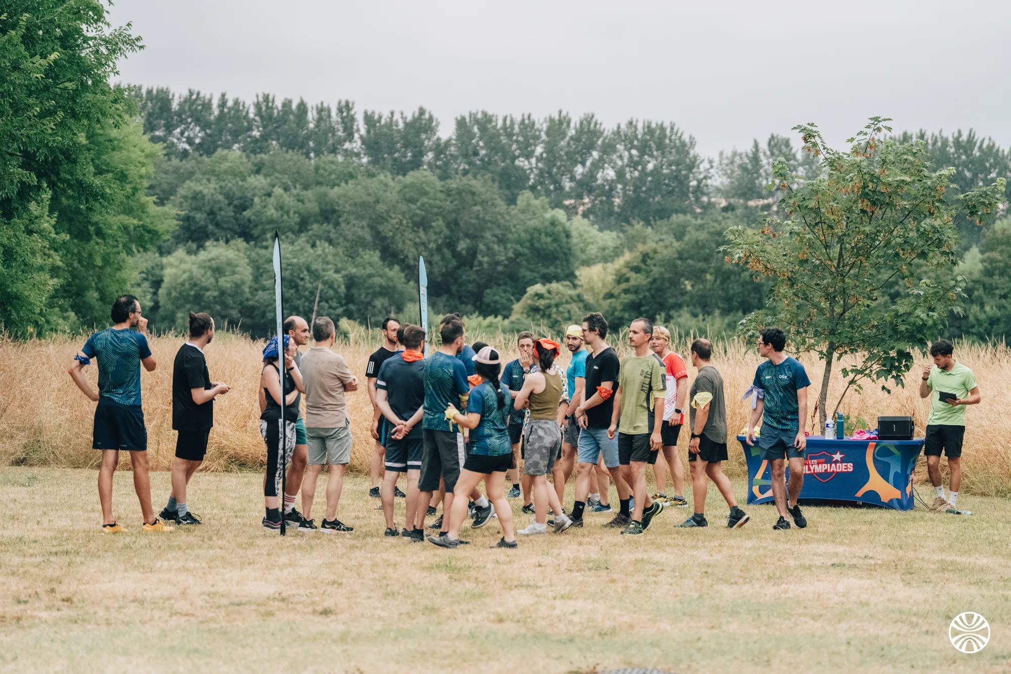 Groupe de personnes en tenues de sport se réunissant sur une pelouse herbeuse avec des arbres en arrière-plan lors d'un événement en plein air.