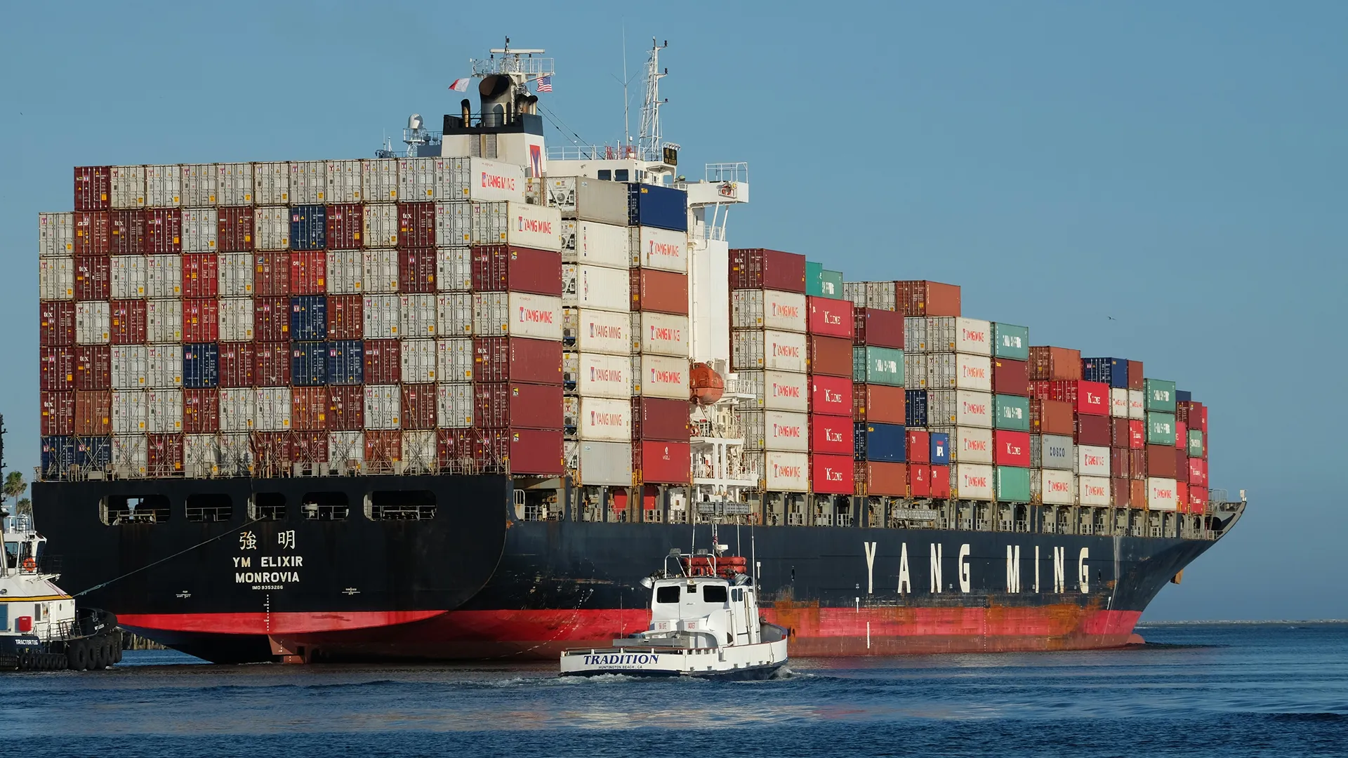 Grand porte-conteneurs Yang Ming chargé de nombreux conteneurs colorés sur l'eau calme sous un ciel clair.