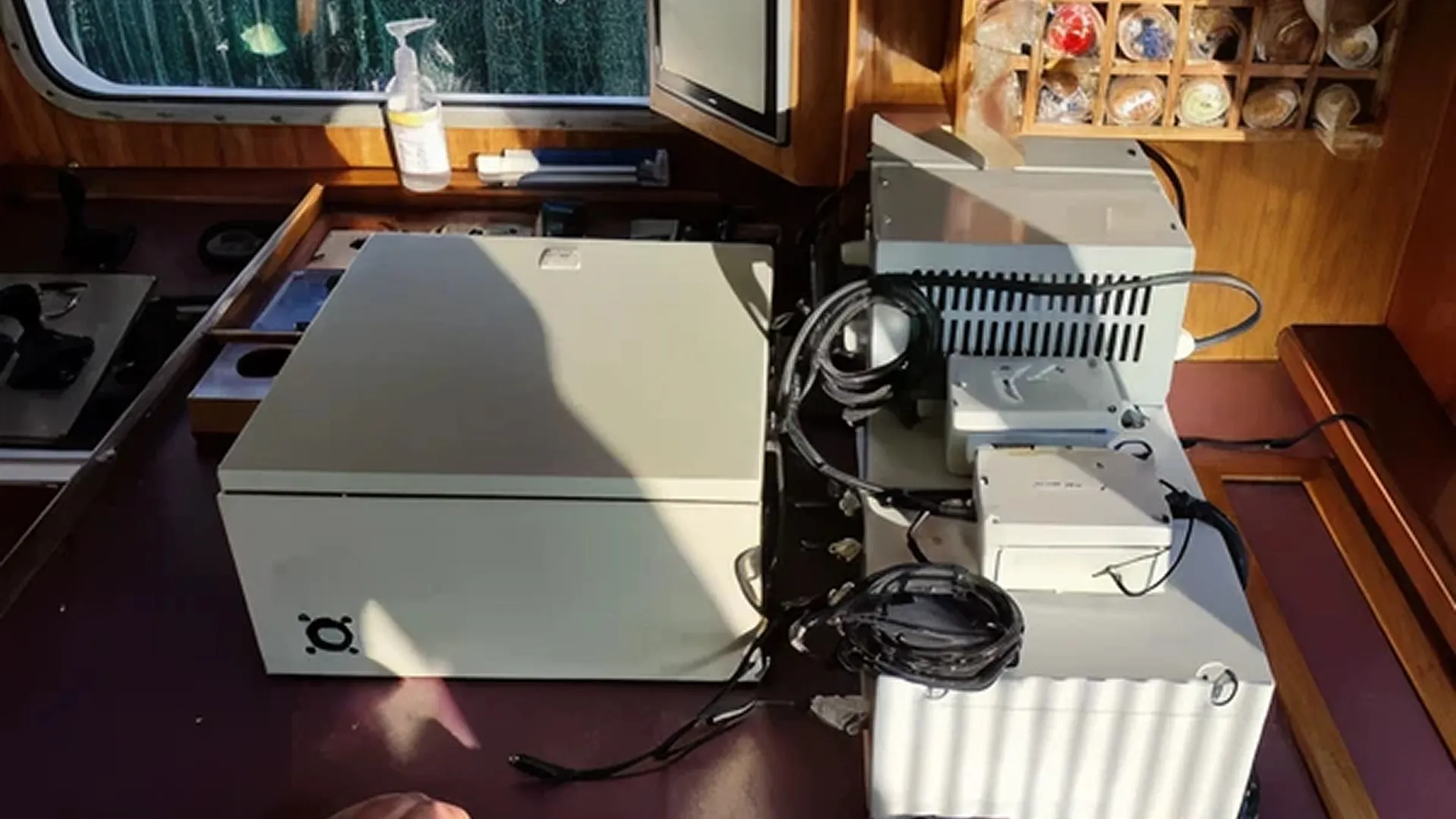 Two large white machines placed on a brown surface in a wooden room with a window and a disinfectant gel dispenser.