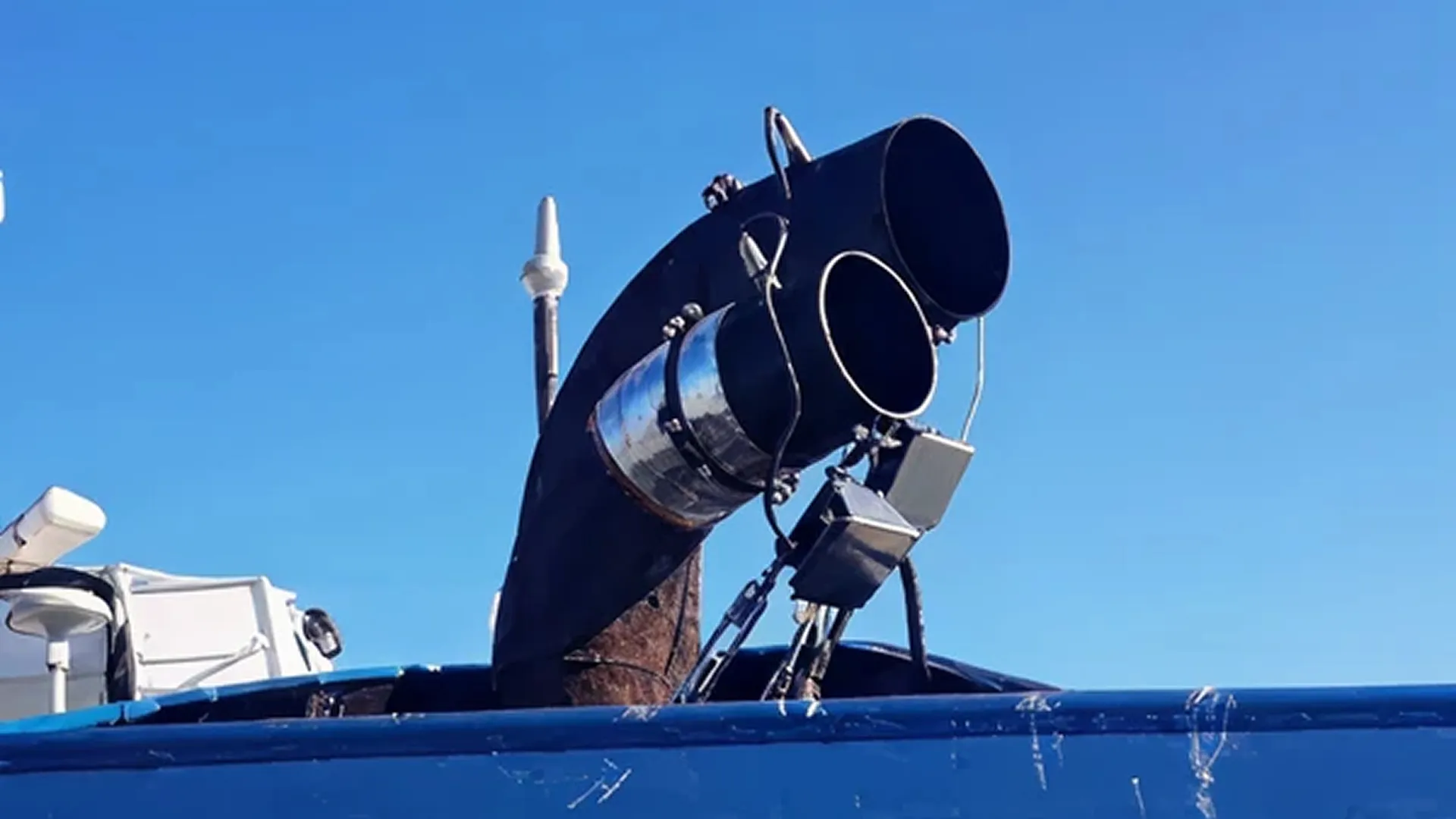 Two large black exhaust chimneys on a blue ship under a clear blue sky.