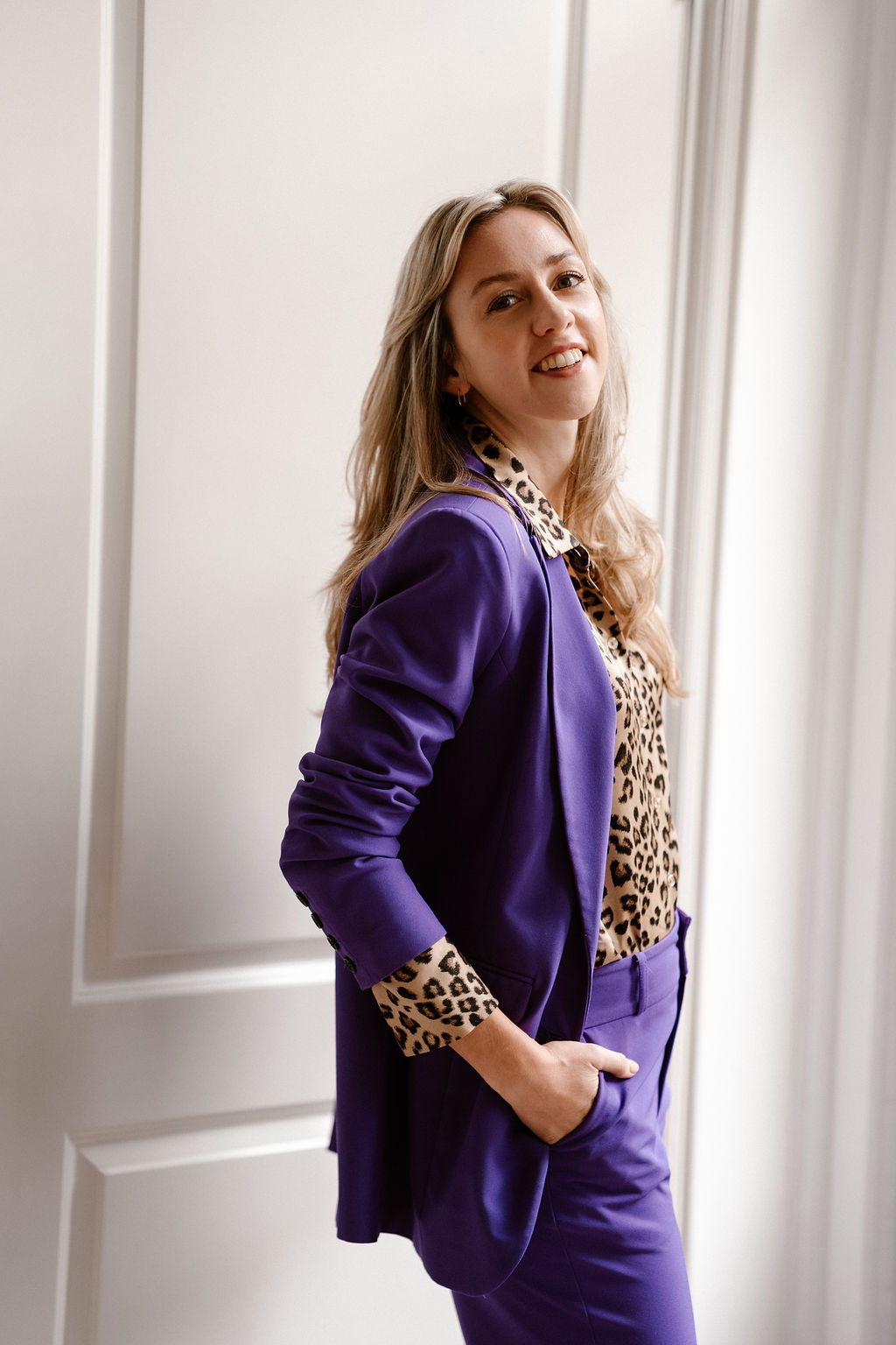 Foto van Jasmijn Tuit die lachend de camera inkijkt, gekleed in een paars pak