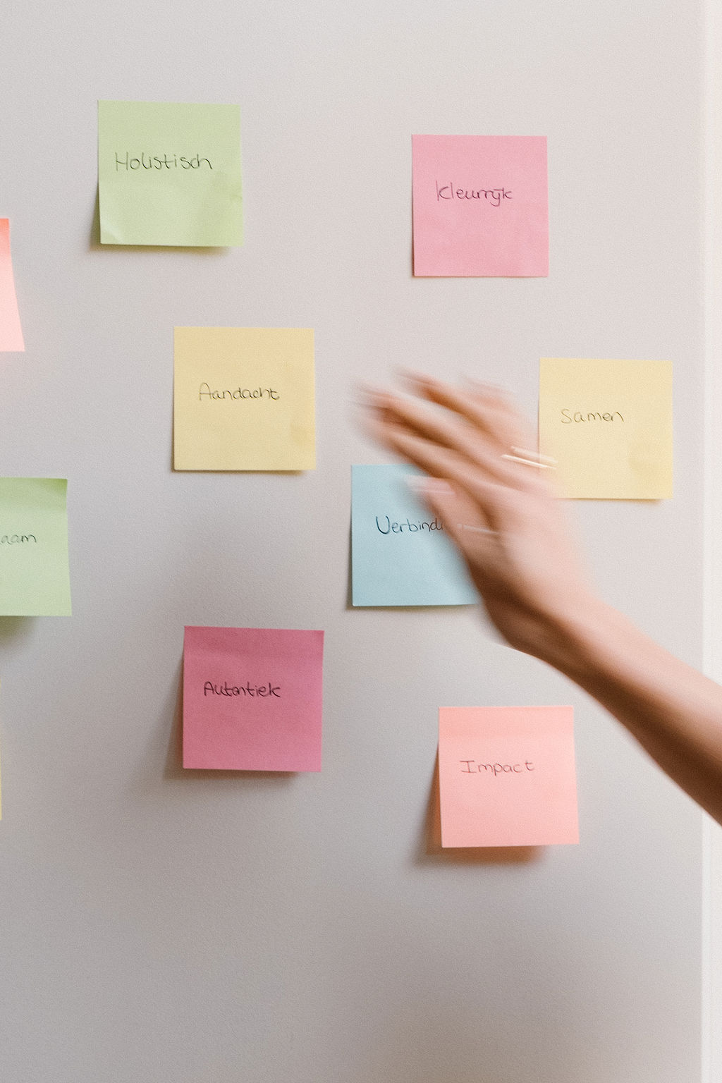Foto van een hand die beweegt voor een muur met post-its