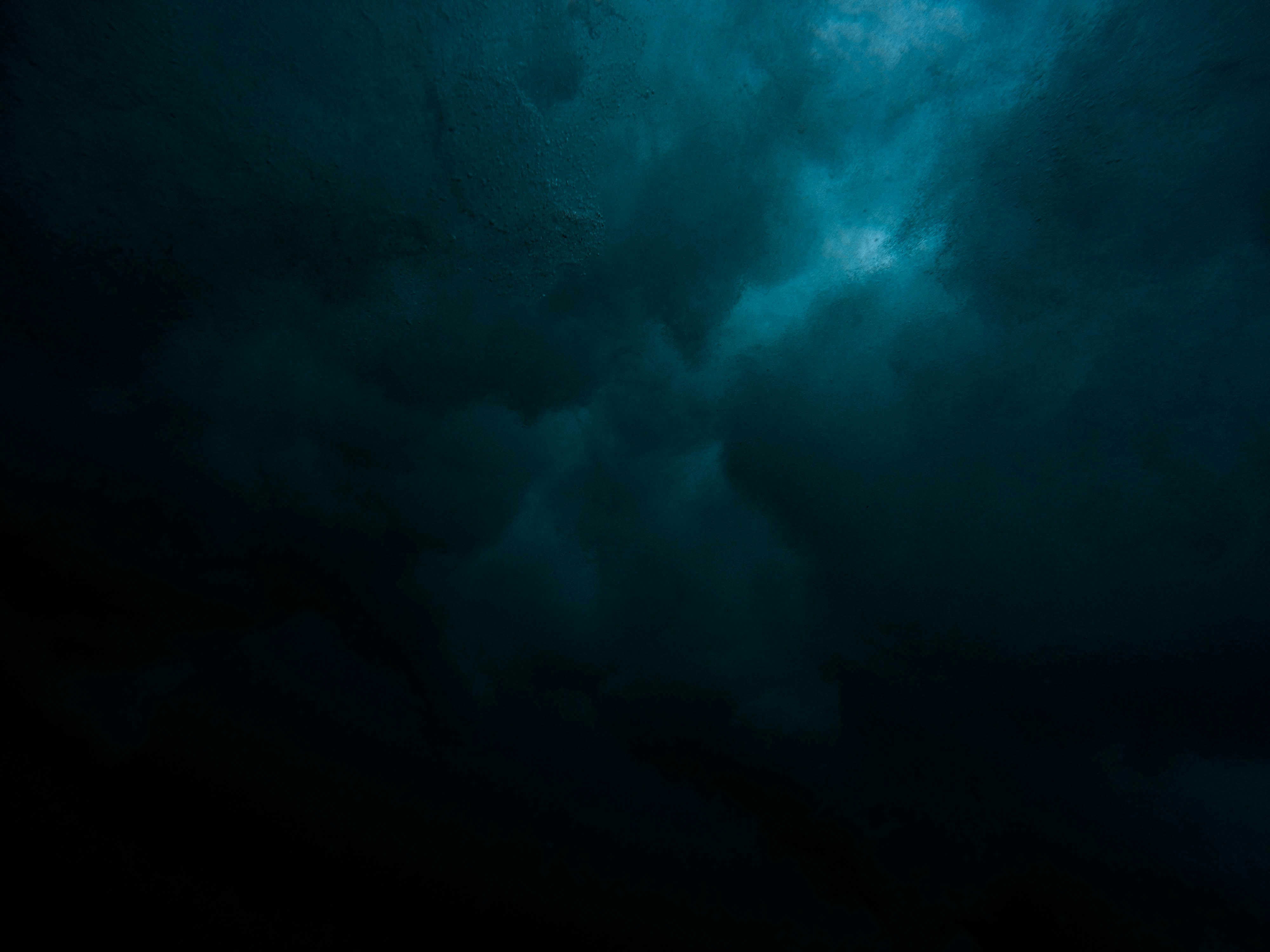 Dark turbulent underwater scene with swirling water and bubbles illuminated by faint blue light.