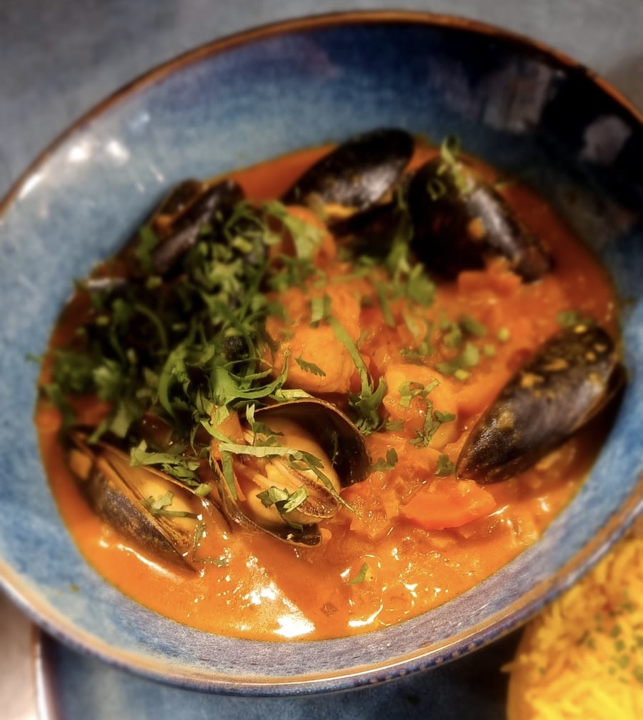 Blue bowl filled with creamy tomato-based seafood stew containing mussels and garnished with chopped herbs.