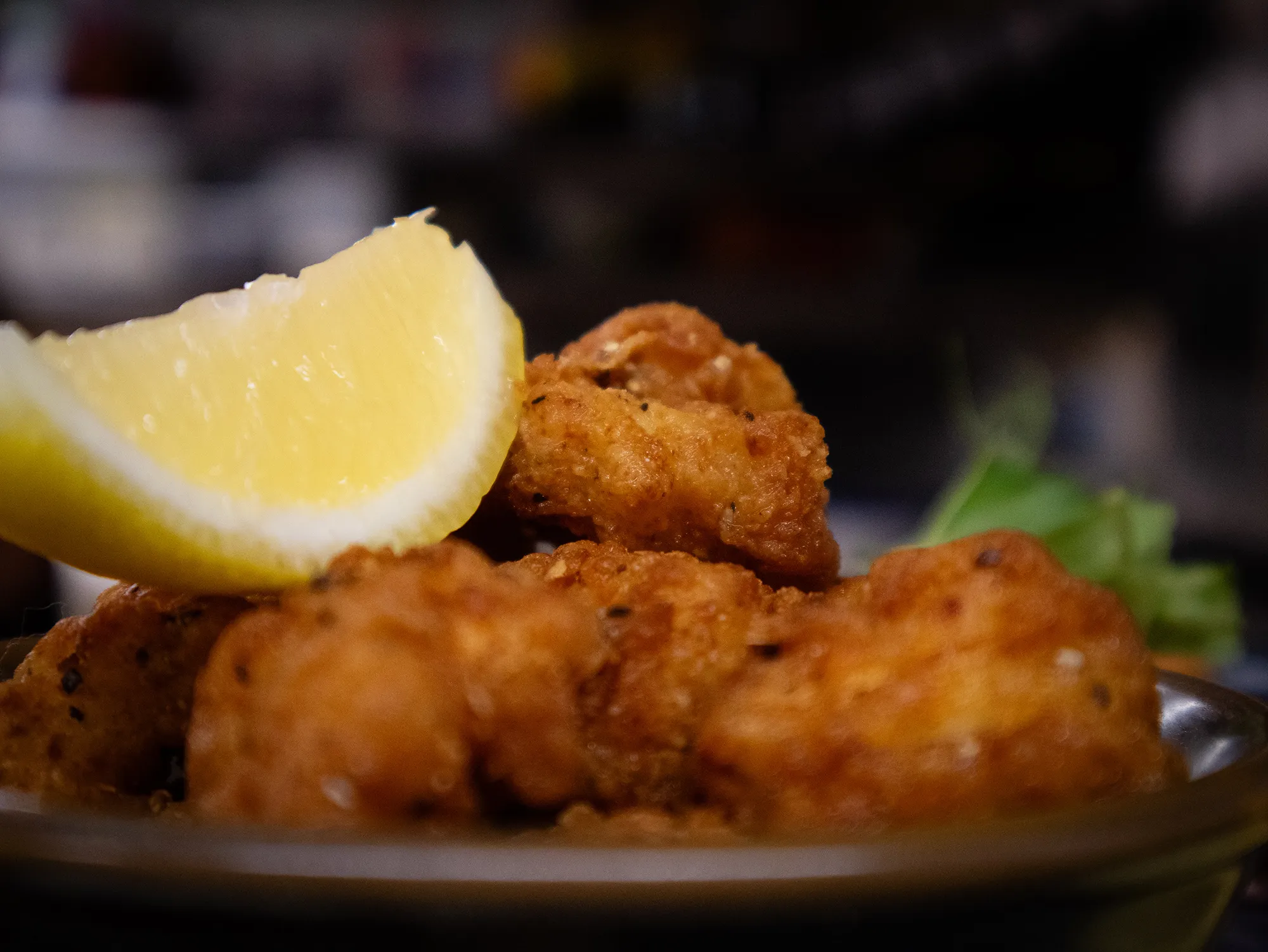 Plate of crispy fried chicken bites garnished with a wedge of lemon and a small green herb.