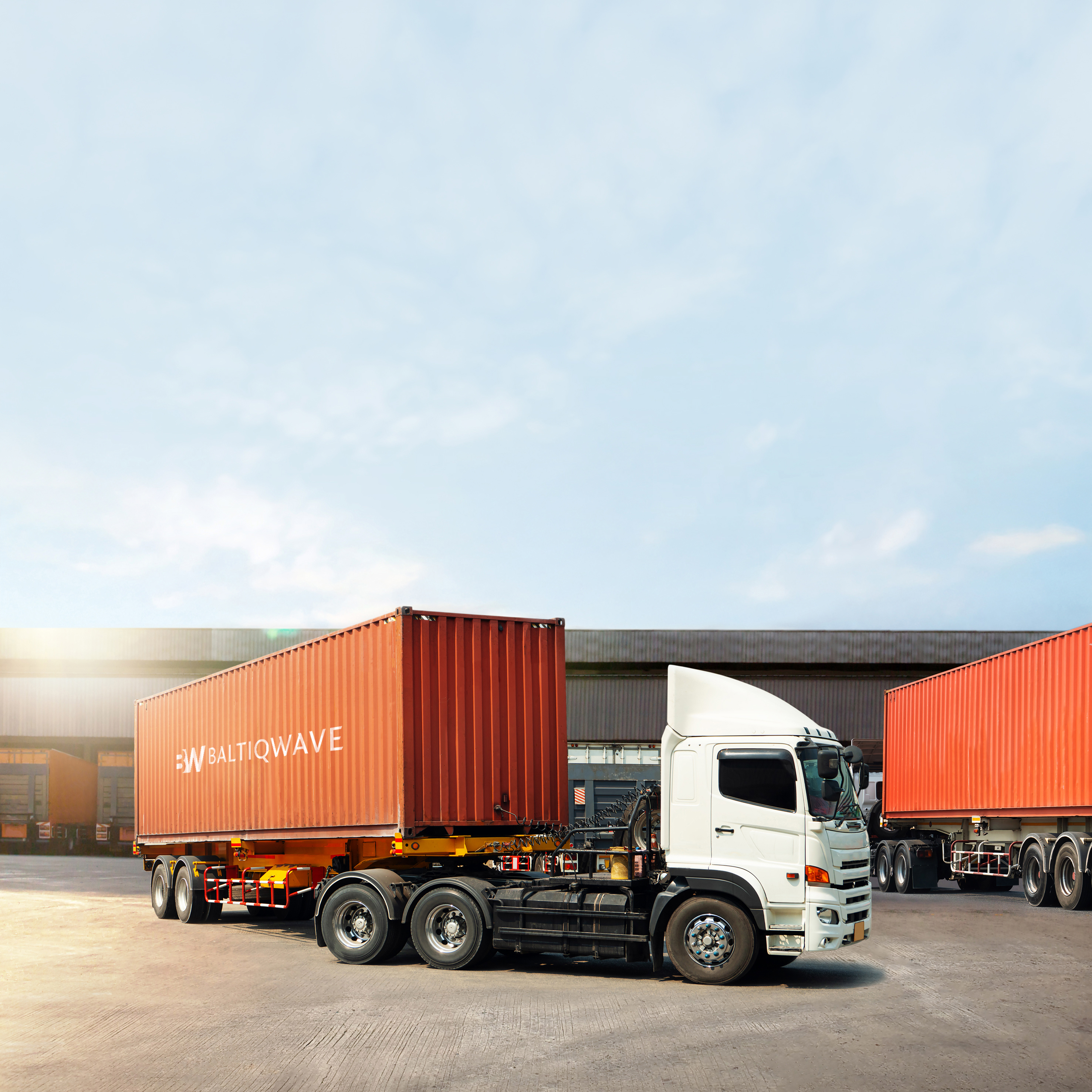 White semi-truck with a red shipping container labeled 'BALTIQWAVE' parked in an industrial area beside another container.