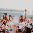 Two young women cheering and enjoying at a crowded outdoor event.