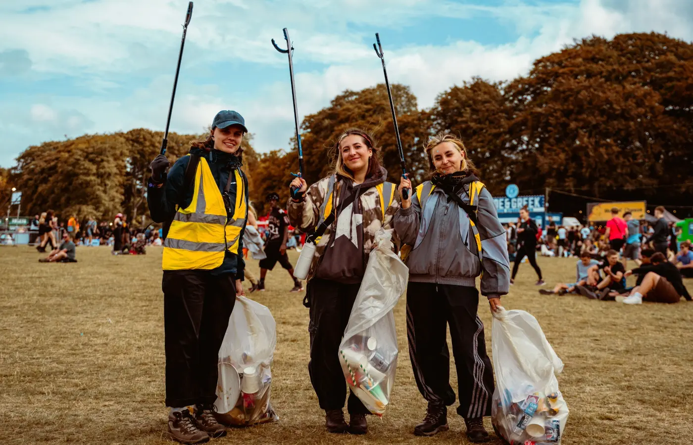 Three young girls wearing green High Vis picking up trash around a green field