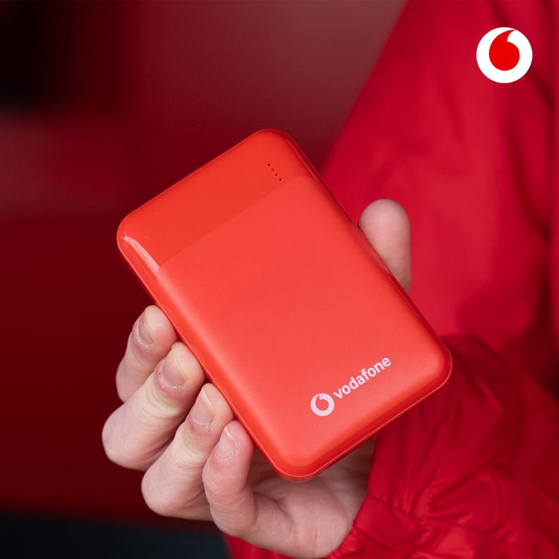 A hand holds a red power bank featuring 'vodafone' and "powered by chargecandy" logo