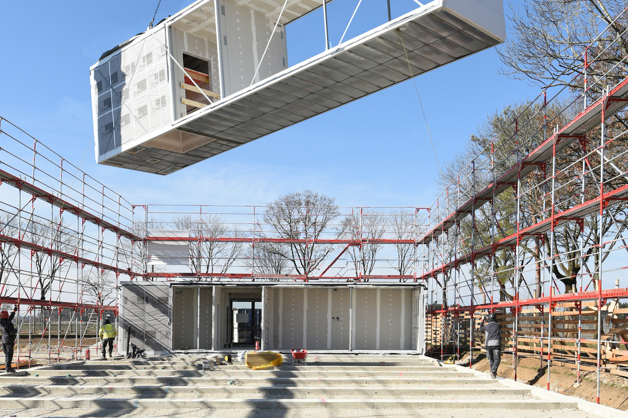 Ein vorgefertigtes, modulares Hausmodul wird mit einem Kran auf eine Baustelle gehoben, um es auf dem Fundament zu platzieren.
