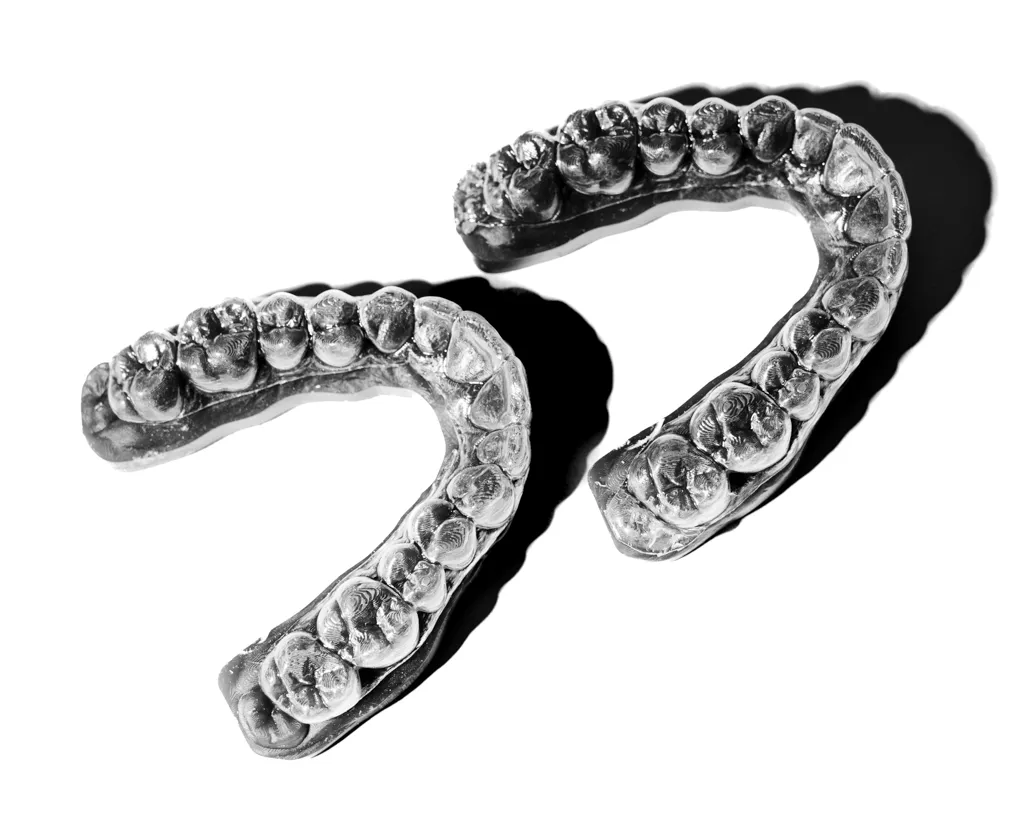 Two clear dental aligner molds of upper and lower teeth on a white background with shadows.