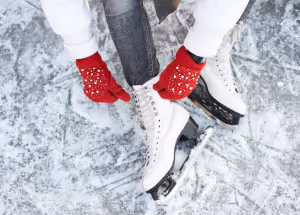 a view of a person in red mittens sitting on an ice rink tying the laces of ice skates