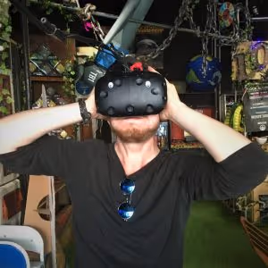 Person in Lockhouse Escape Games foyer with a Vive VR headset on, with googly eyes, clutching his head