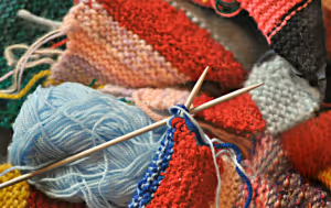 knitting needles with some multicoloured knitting on top of colorful blue and red yarn