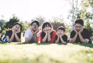 a family lying on grass smiling at the camera with their chins in their hands