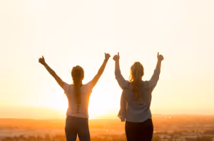 two people with their backs to the camera doing double thumbs up against the sunset